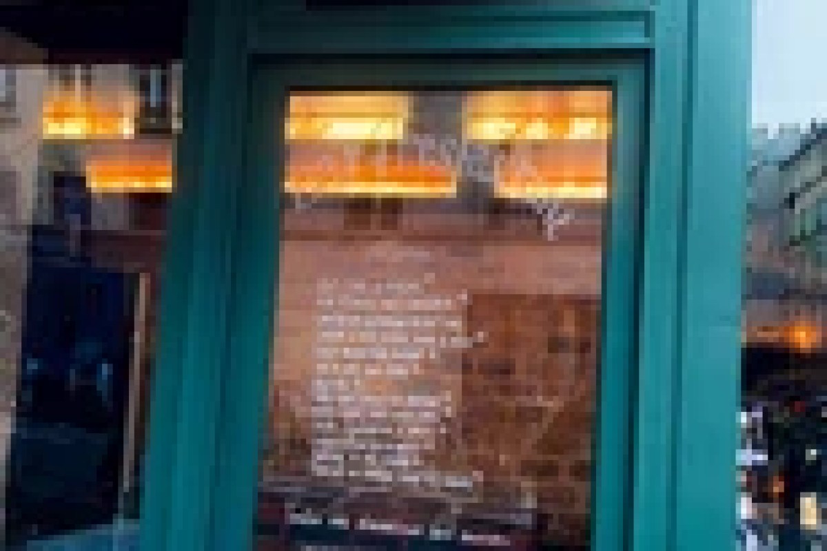Restaurant storefront with teal window frame and menu posted, warm interior lighting visible through glass