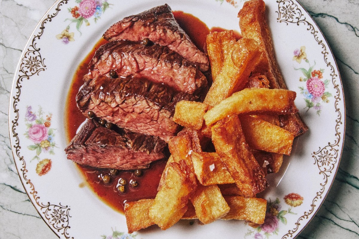 Sliced steak with peppercorn sauce and crispy chips on a floral-rimmed plate