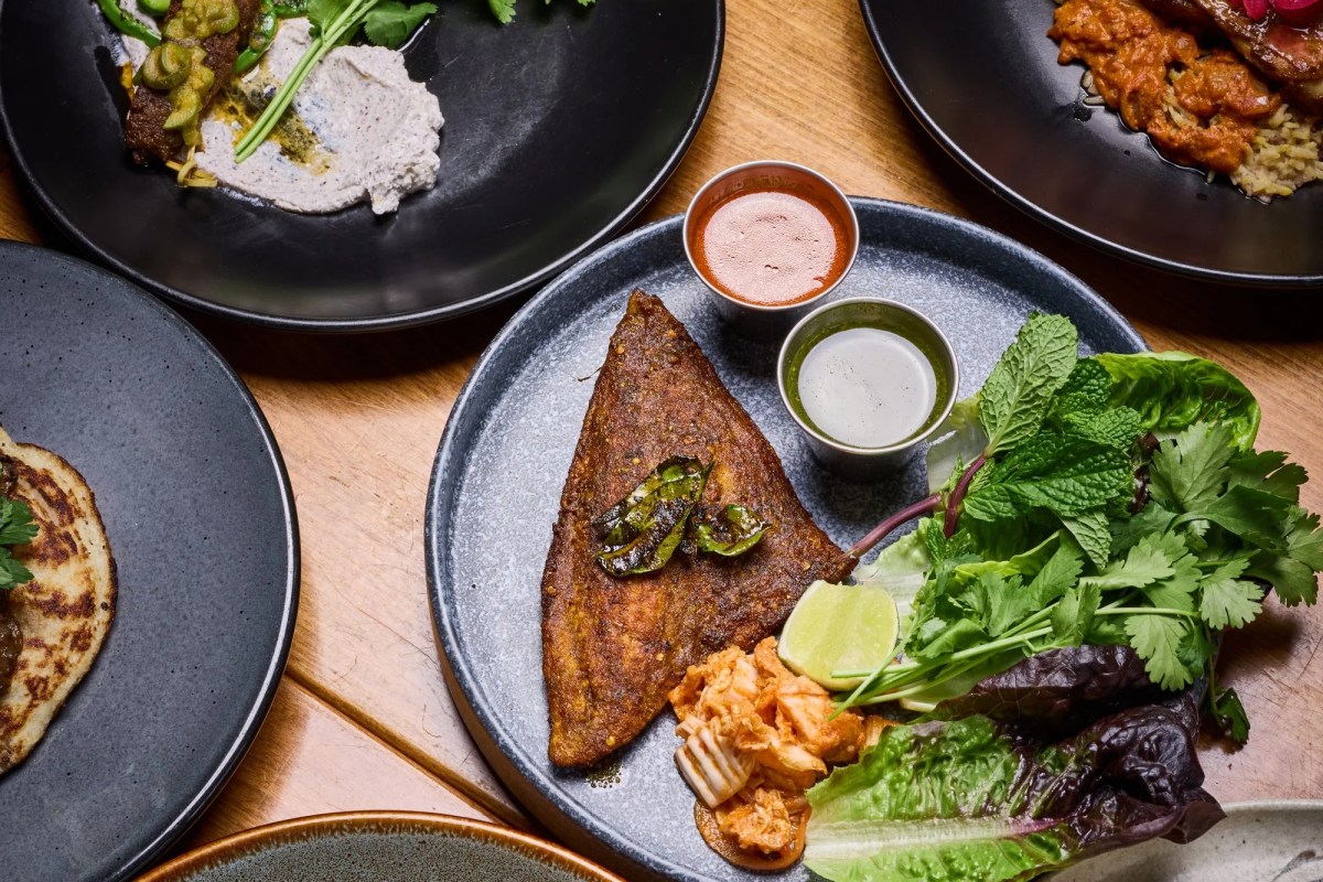 Overhead shot of multiple plated dishes on wooden table including spiced fish and curry
