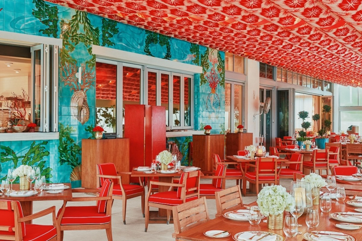 Restaurant terrace with blue tiled wall, red patterned awning, and red chairs at set tables