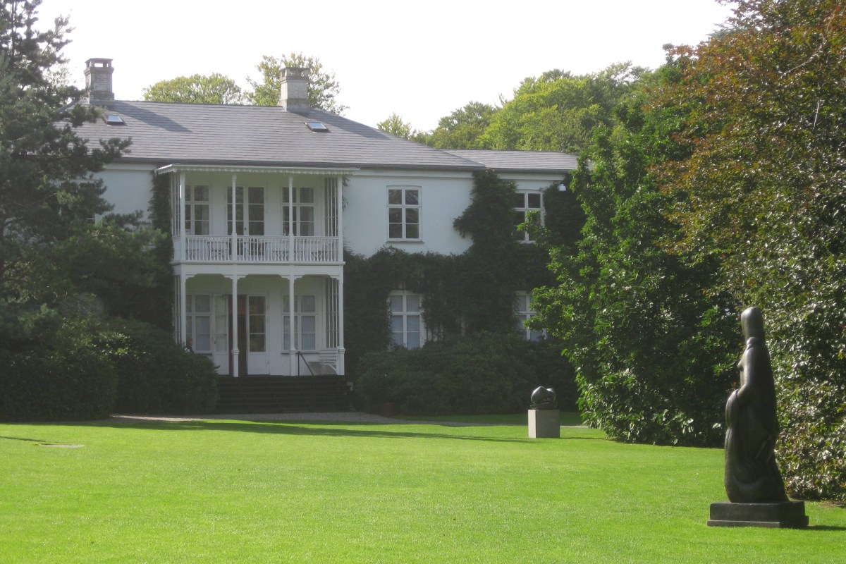 White ivy-covered villa seen across a lawn with a modern bronze sculpture in foreground