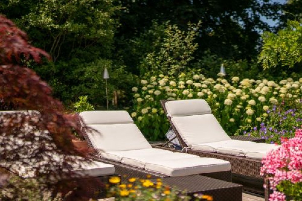 Two cushioned sun loungers on a terrace surrounded by lush garden flowers and hydrangeas