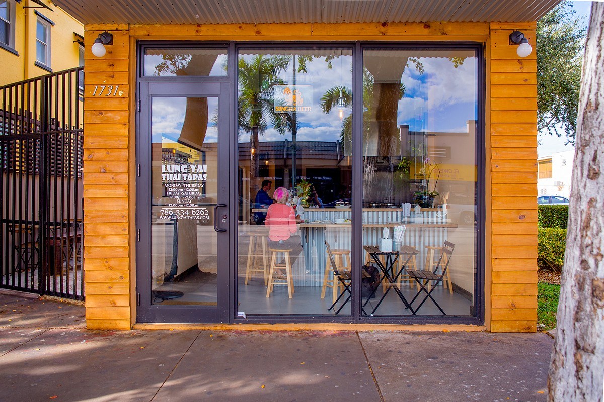 Exterior storefront of Lung Yai Thai Tapas with wood paneling, glass windows showing interior seating and a patron
