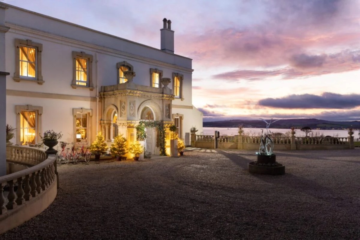 Lympstone Manor's illuminated façade at dusk with estuary views and sunset sky in the background