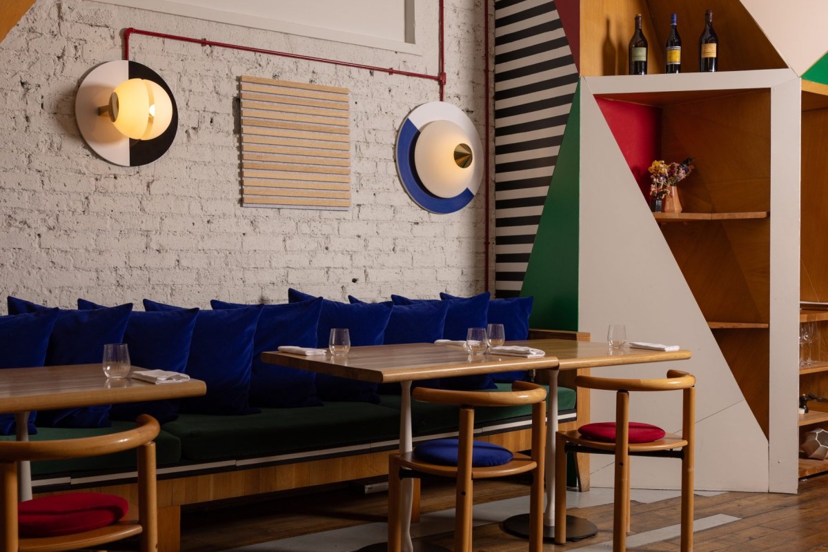 Restaurant dining room with blue velvet banquette, wooden tables and geometric colorful wall art