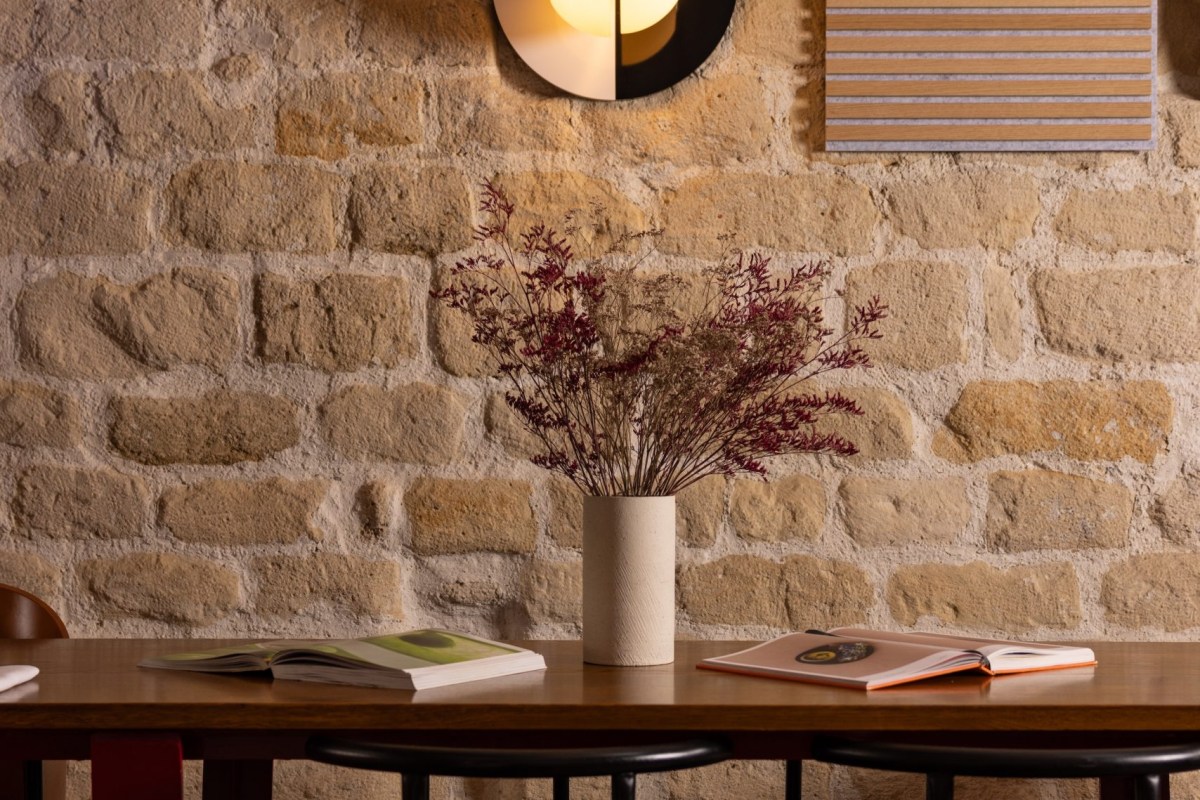 Stone wall with wooden table, vase of dried flowers and open books, dim lighting