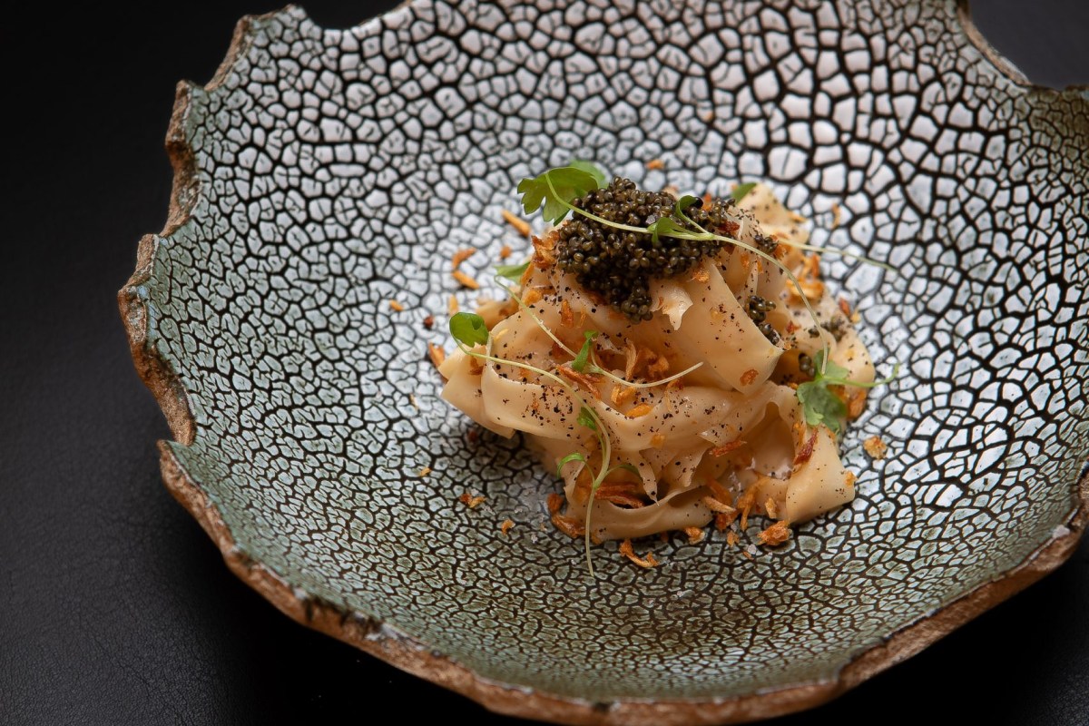 Textured ceramic bowl with pasta or seafood topped with caviar and herbs
