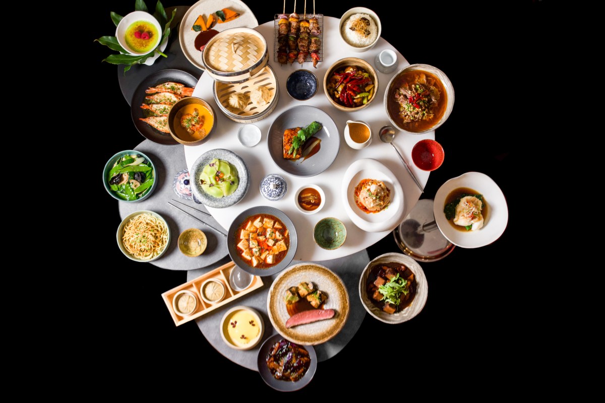 Overhead view of a round table filled with assorted Asian dishes, dim sum, skewers, and small bowls at Madame FAN