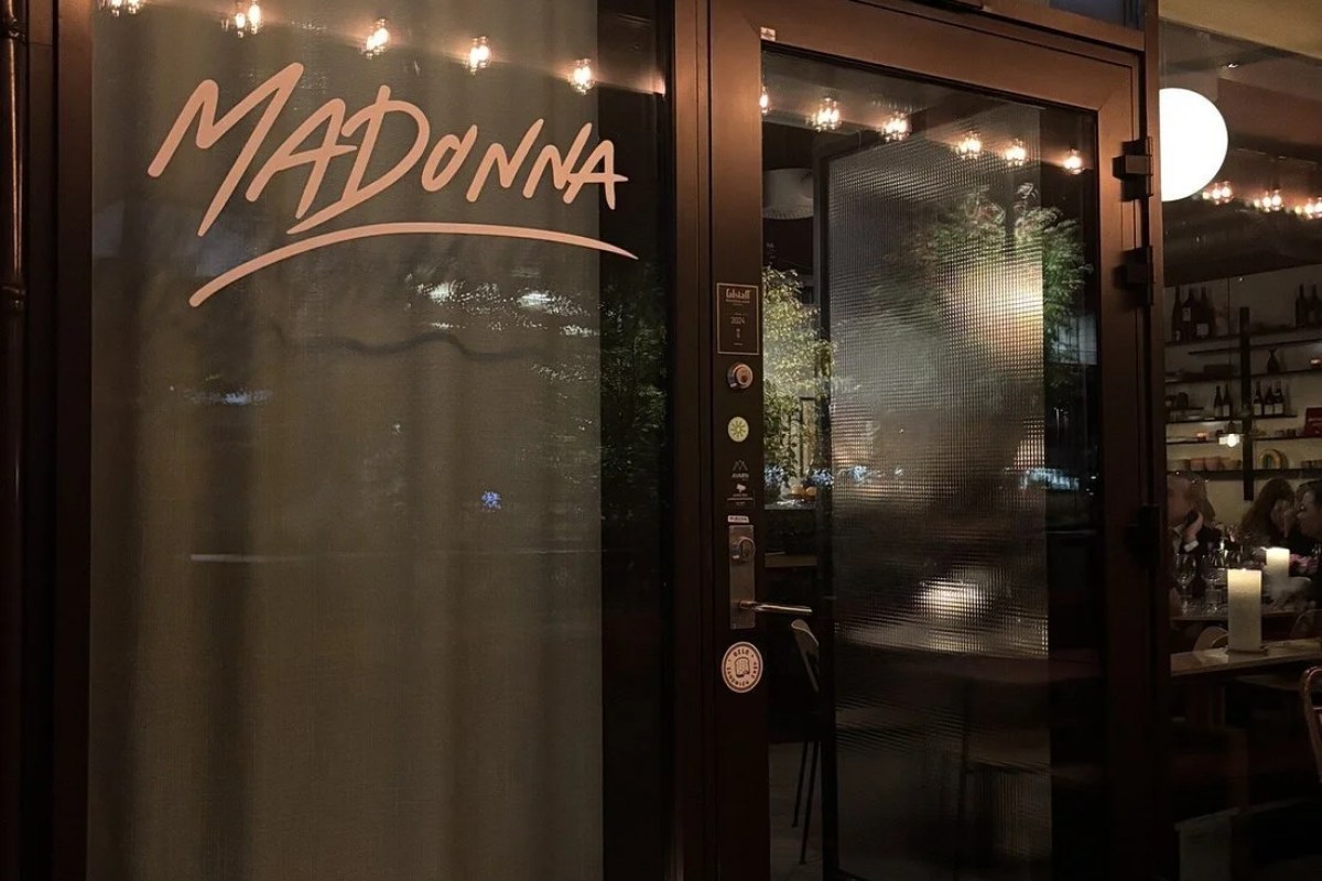 Restaurant exterior entrance at night with Madonna sign on glass door and string lights