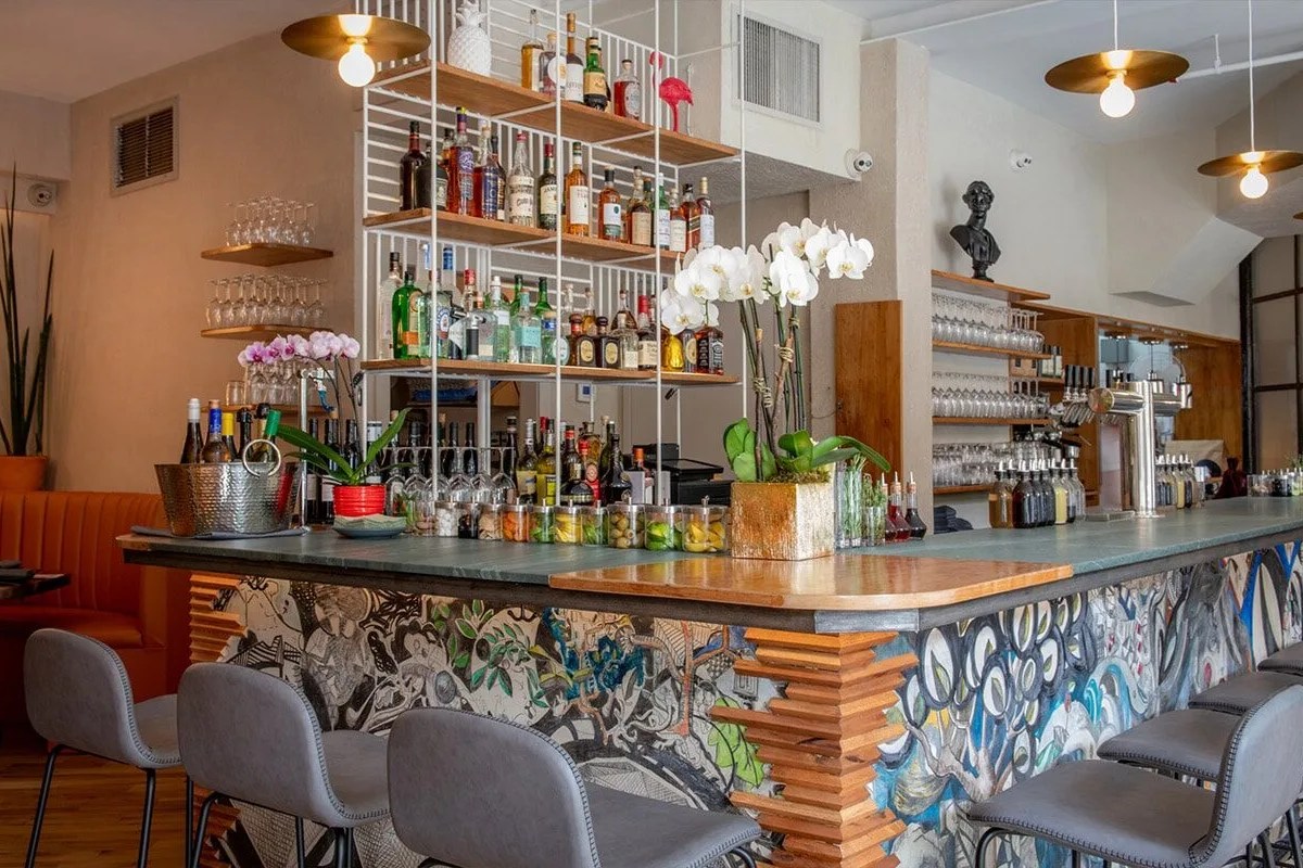 Restaurant bar with shelved liquor bottles, orchids, and colorful painted bar front