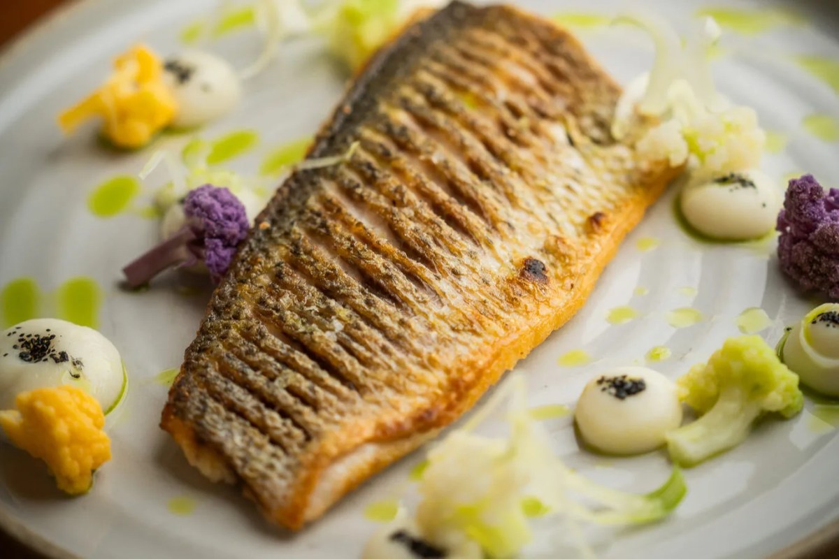Plated crispy-skinned fish fillet with colorful vegetable garnishes