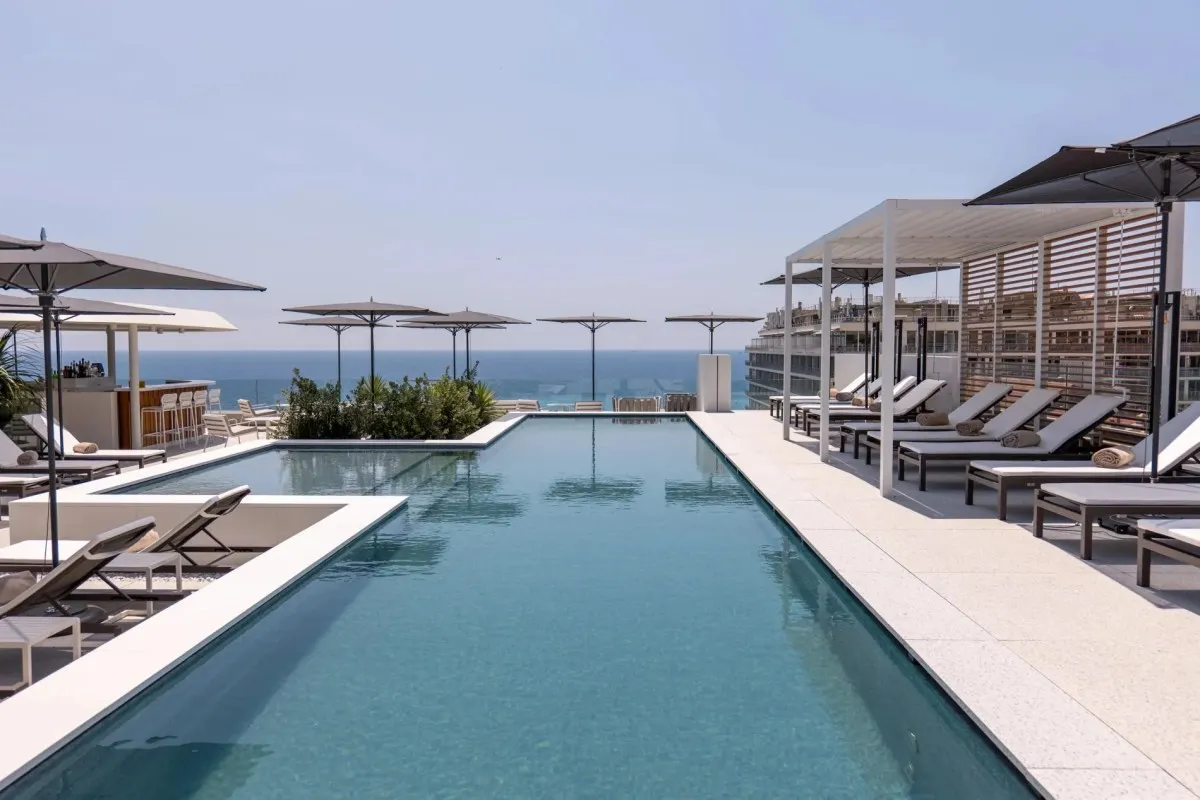 Rooftop infinity pool with loungers and umbrellas, the hotel building visible alongside, overlooking the Mediterranean Sea