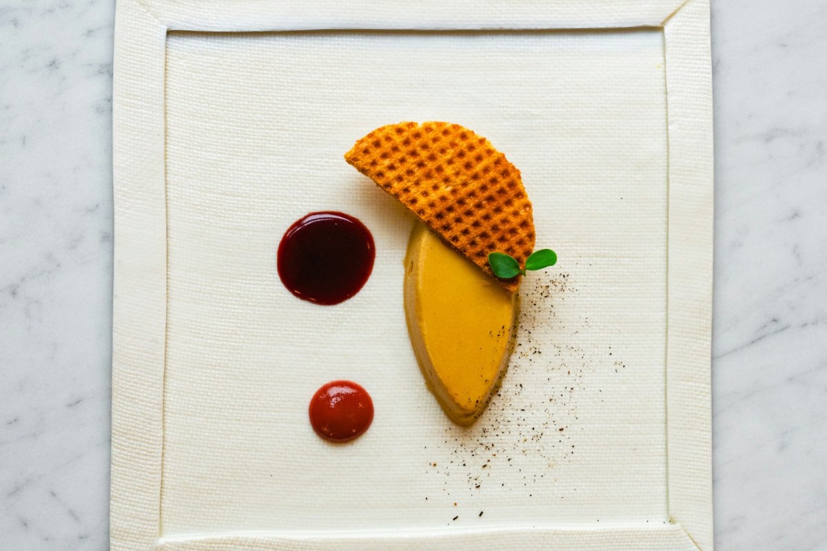 Foie gras slice with waffle tuile and two sauce dots on a square white plate