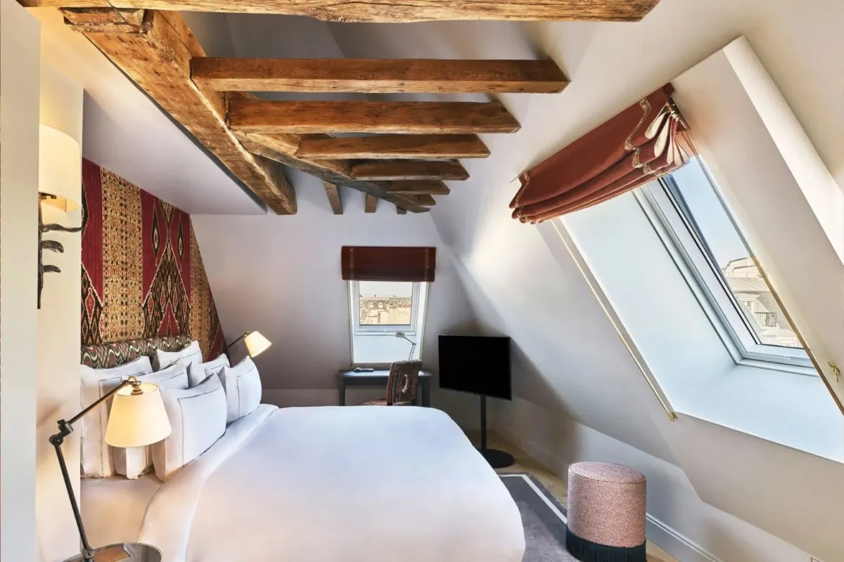 Attic guest room with wood beams, skylight window, white bed and red textile headboard
