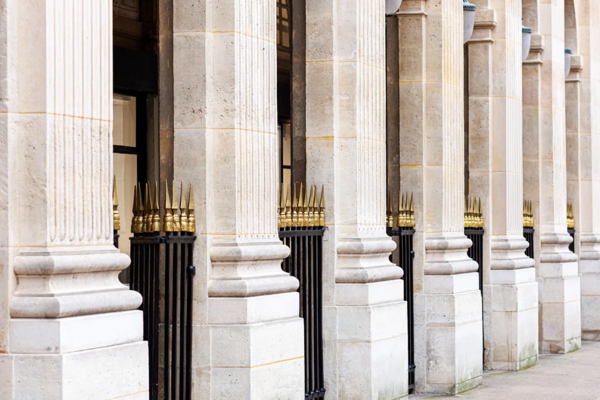 Close-up of the classical stone colonnade with gilded fence spikes at the Palais Royal arcade.
