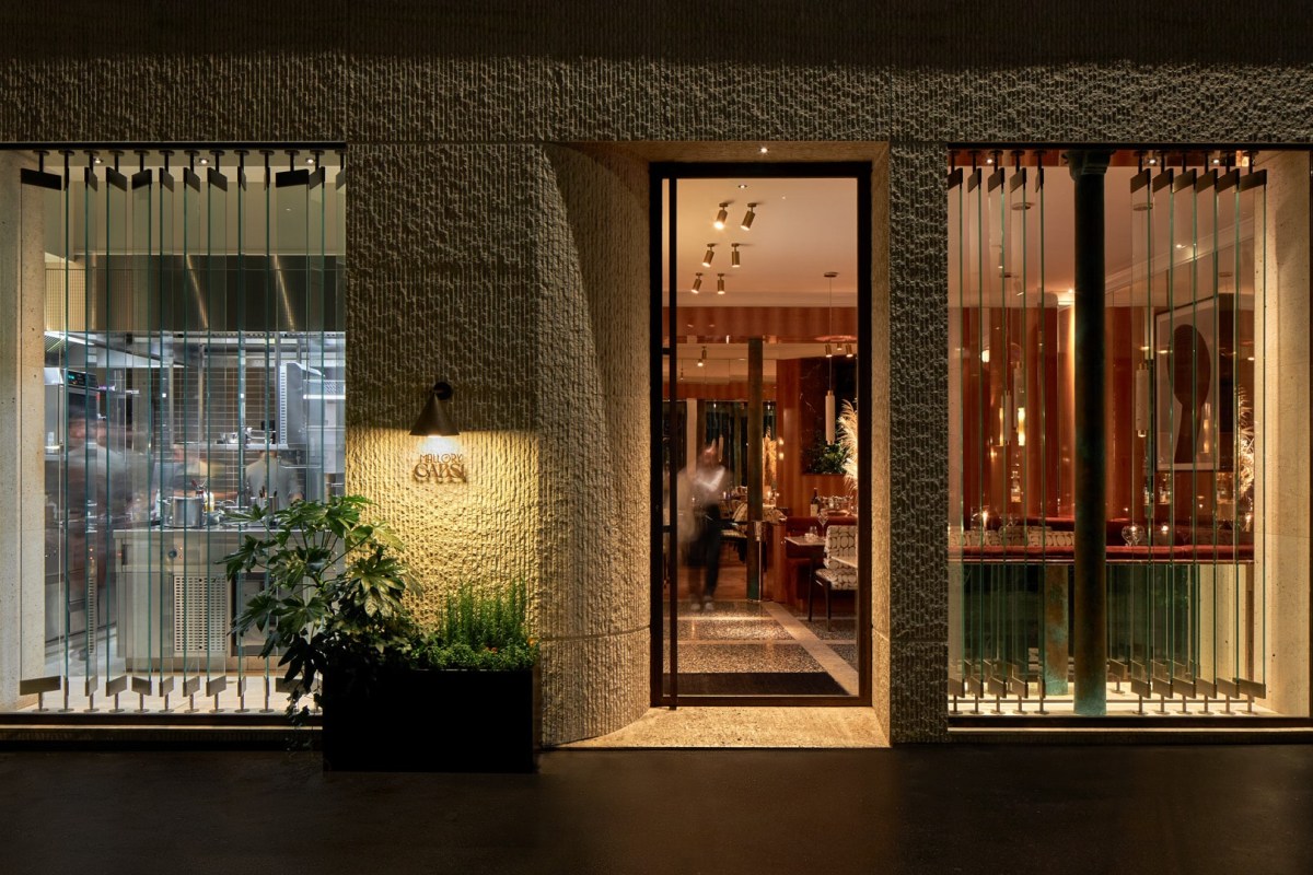 Restaurant exterior at night with glass entrance door and view into warmly lit dining room