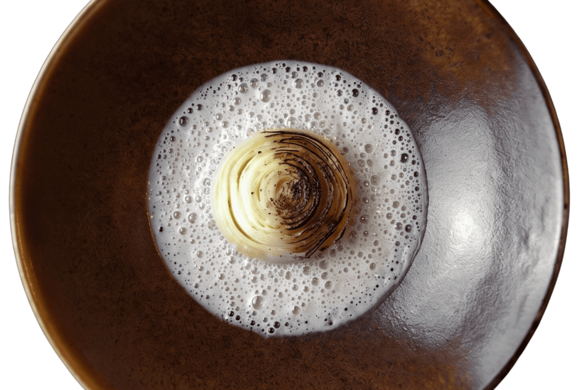 Overhead shot of a dish with charred onion and foam on a dark ceramic plate