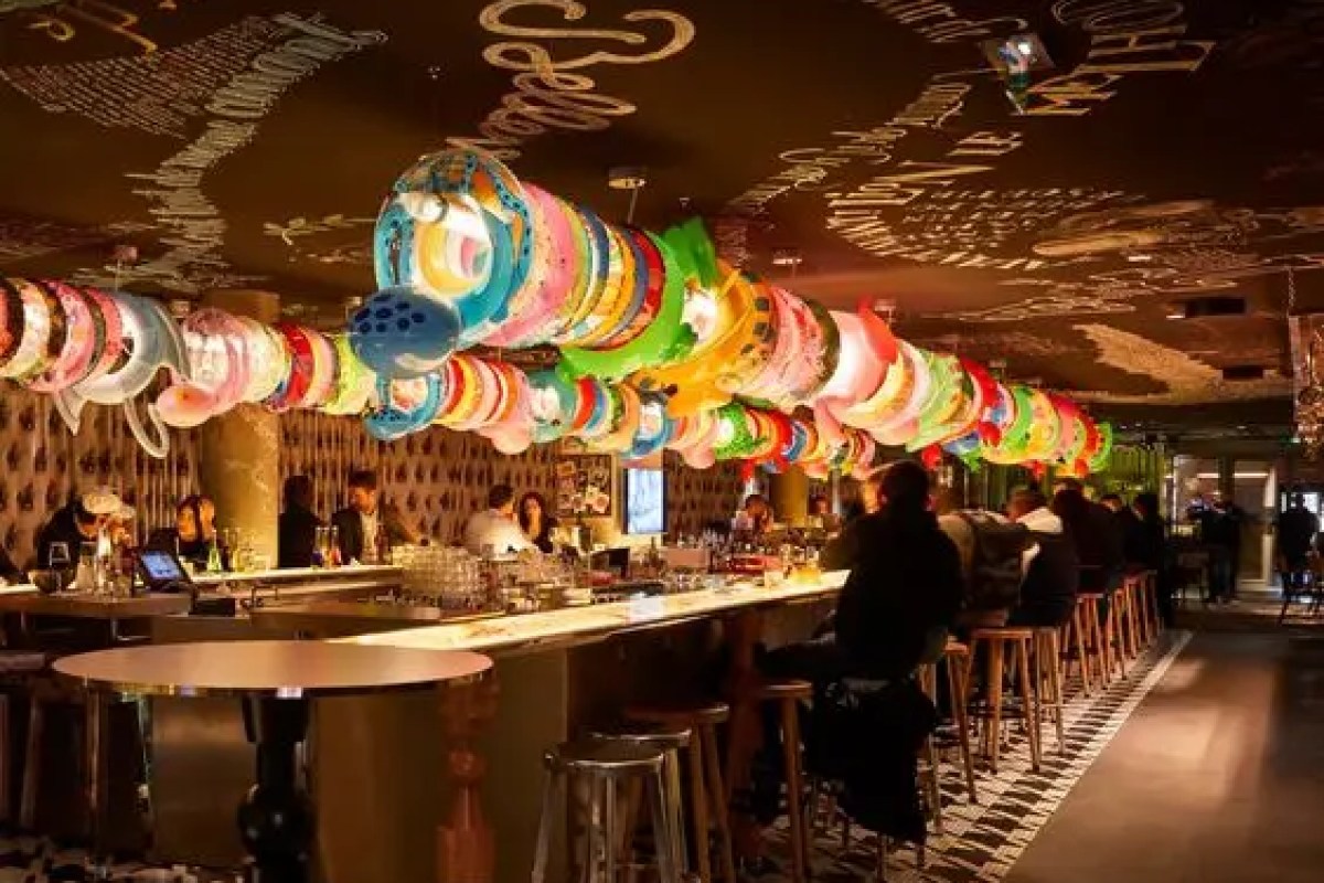Colorful bar lounge with patterned ceiling and guests seated at a long bar counter