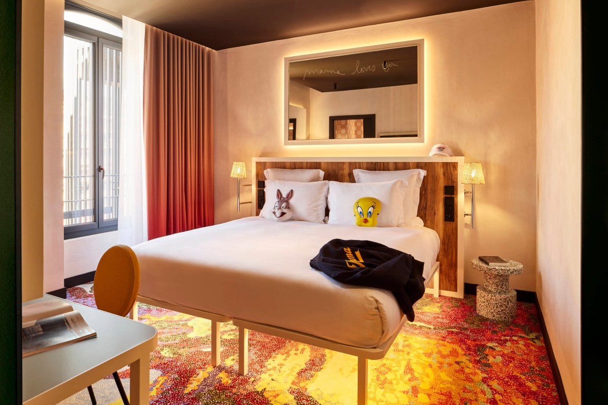 Guest room with wood headboard bed, Looney Tunes plush pillows, red patterned rug, and mirror