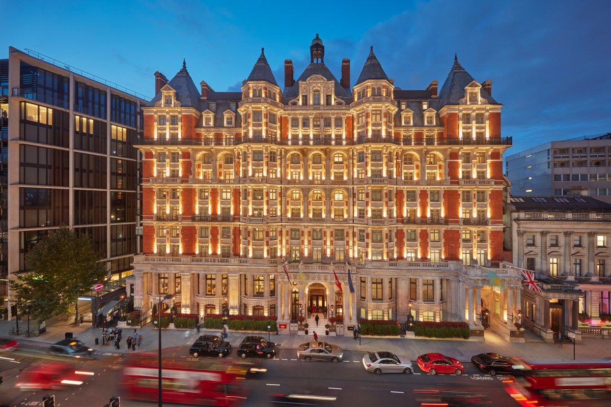 Twilight view of Mandarin Oriental Hyde Park's ornate red-brick facade, illuminated windows, with traffic blurred in front