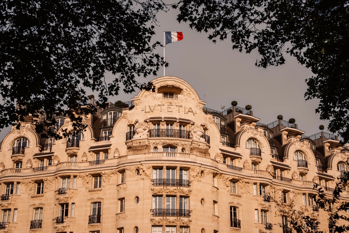 Art Deco façade of Hotel Lutetia with 'LUTETIA' signage and French flag, framed by tree branches