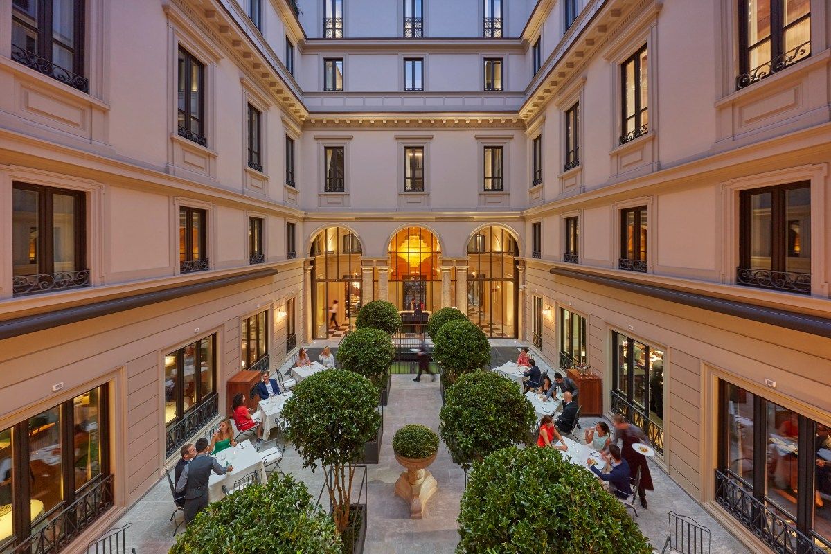 Elegant interior courtyard of Mandarin Oriental Milan with outdoor dining, topiary trees, and classic Milanese architecture