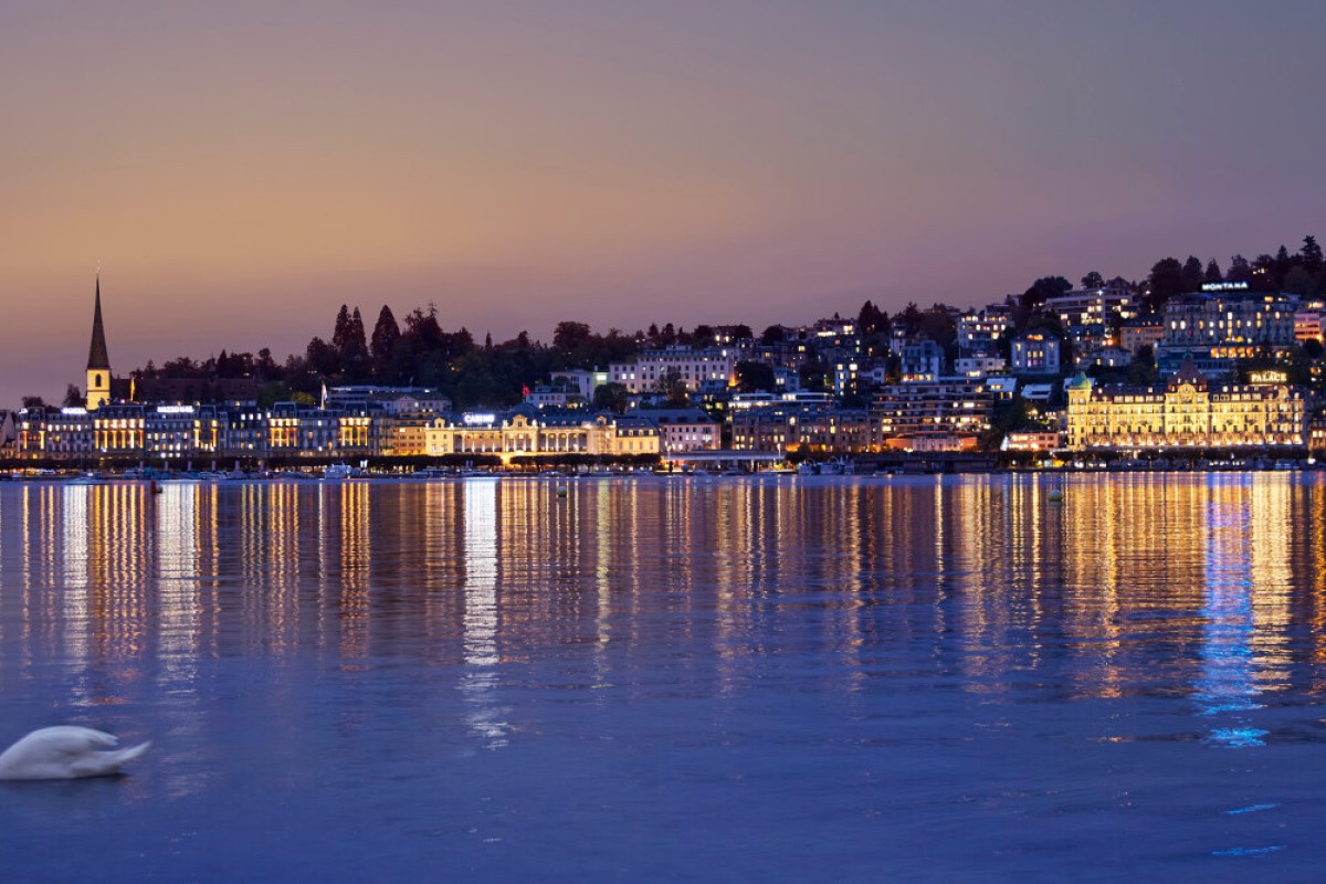 Twilight skyline view of Luzern waterfront with illuminated historic hotel buildings reflecting on the lake, a swan in foreground