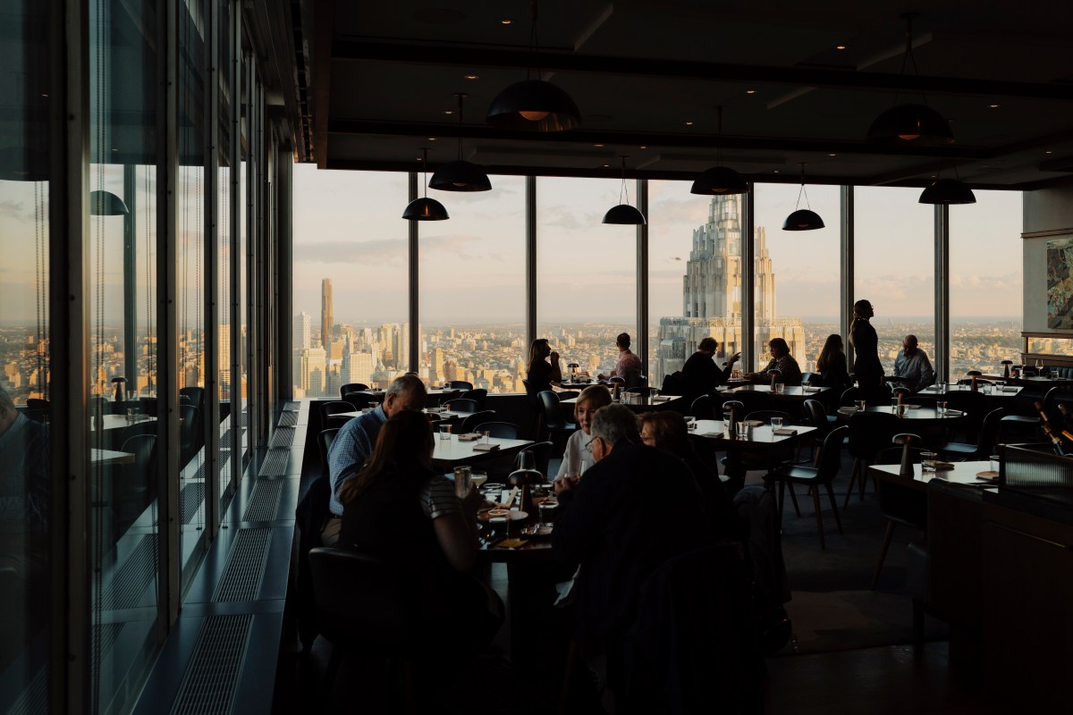 Wide view of dining room with skyline and Art Deco tower visible through large windows, diners seated at tables