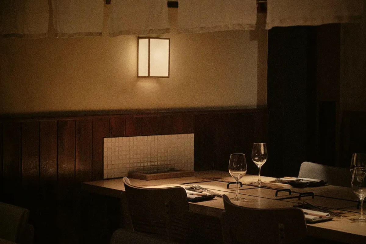 Dim dining room with wooden table, wine glasses, warm lantern light on wall