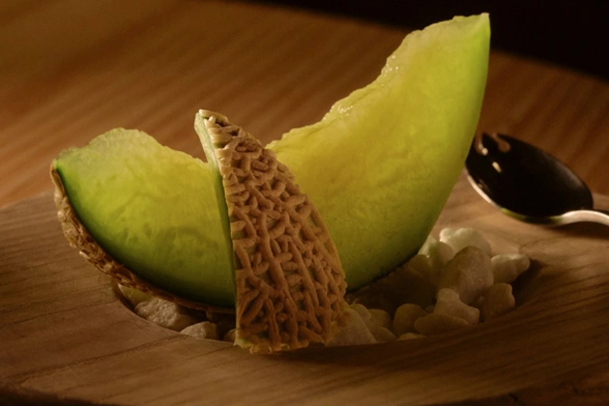 Plated dessert with sliced melon and crisp wafer garnish on wooden board