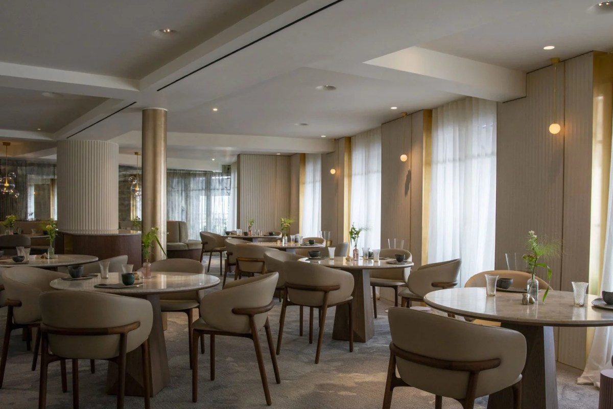 Elegant restaurant dining room with round marble tables, cream chairs, and soft pendant lighting