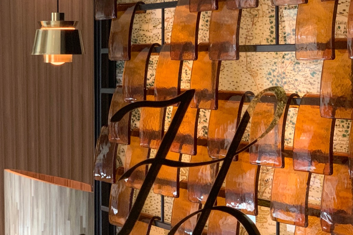 Close-up of decorative amber glass panels and a stylized H monogram against map-patterned wallpaper, restaurant interior detail.