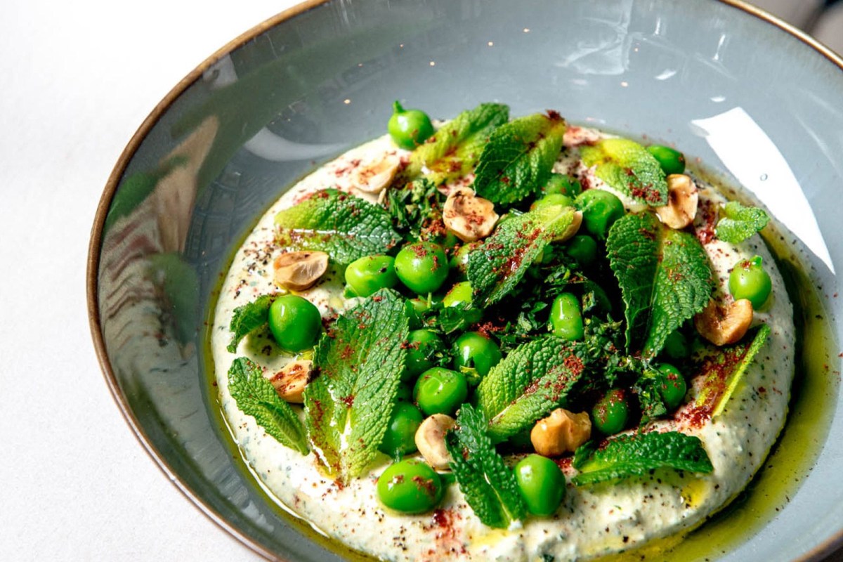 Close-up of a dish with whipped dip topped with green peas, mint leaves, hazelnuts and spices.