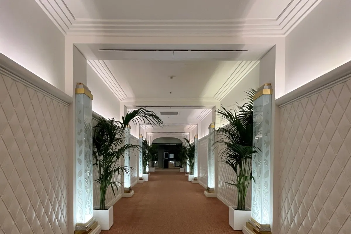 Elegant hotel corridor with palm plants, glowing glass columns and patterned carpet