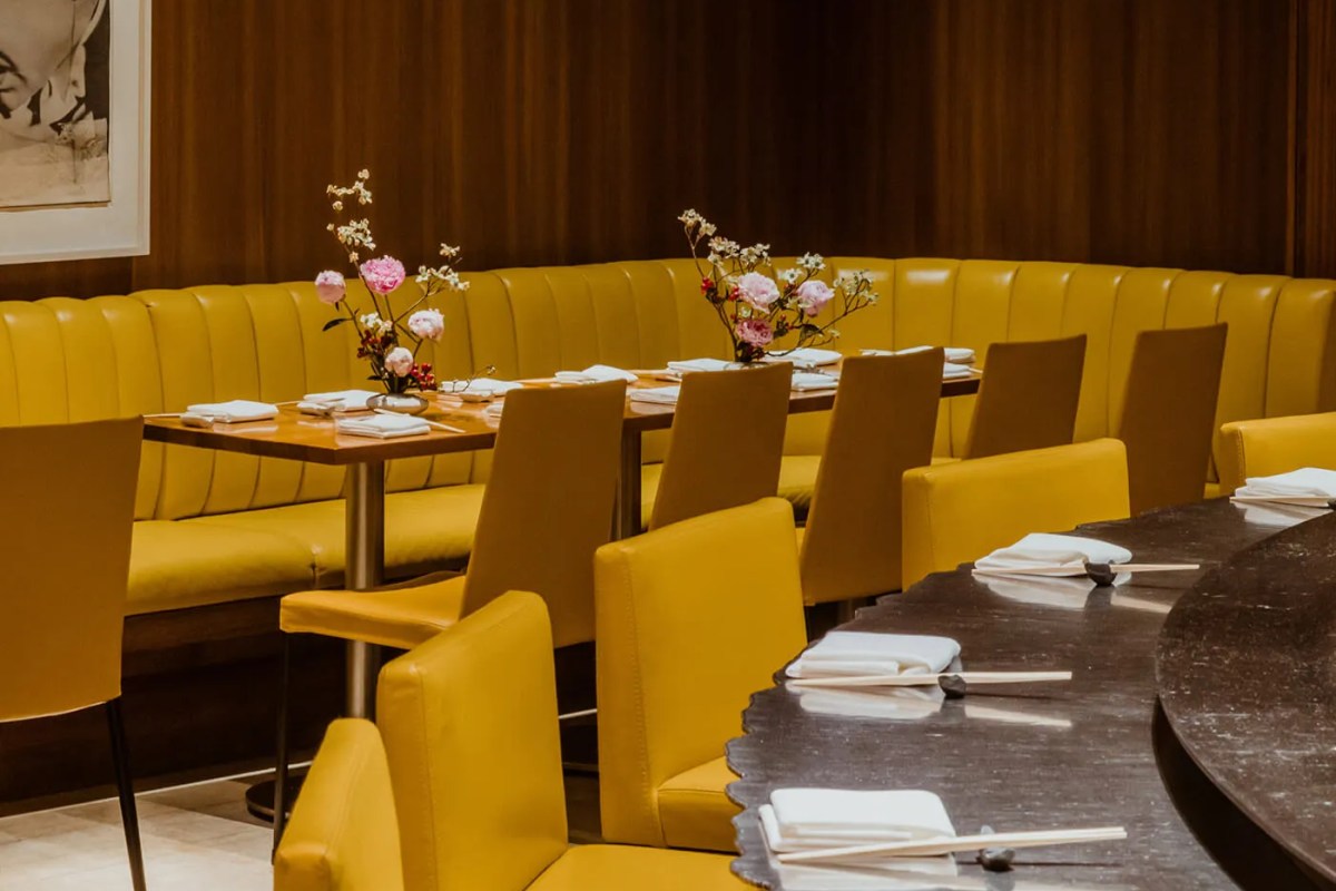 Dining room with yellow leather banquette seating, wood tables set with chopsticks, and floral arrangements.
