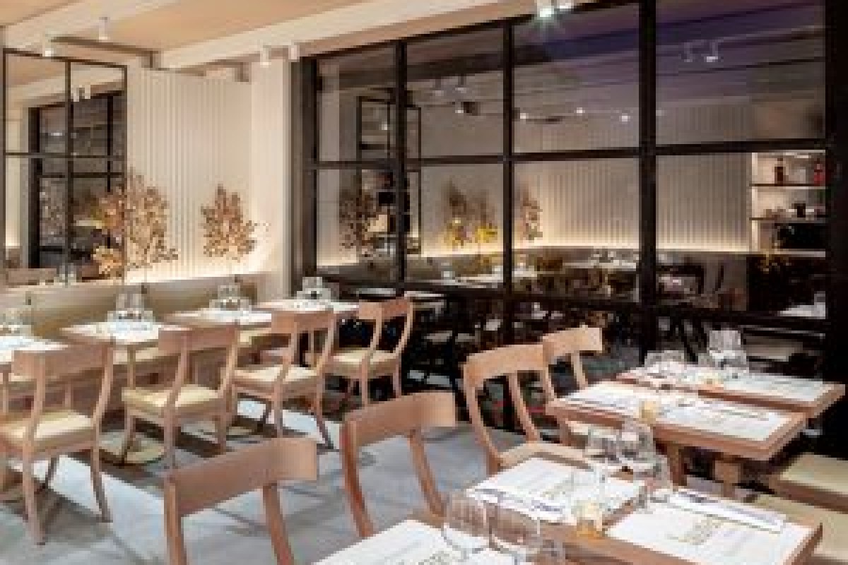Modern restaurant dining room with wooden chairs, set tables, large black-framed windows and gold branch decor at dusk