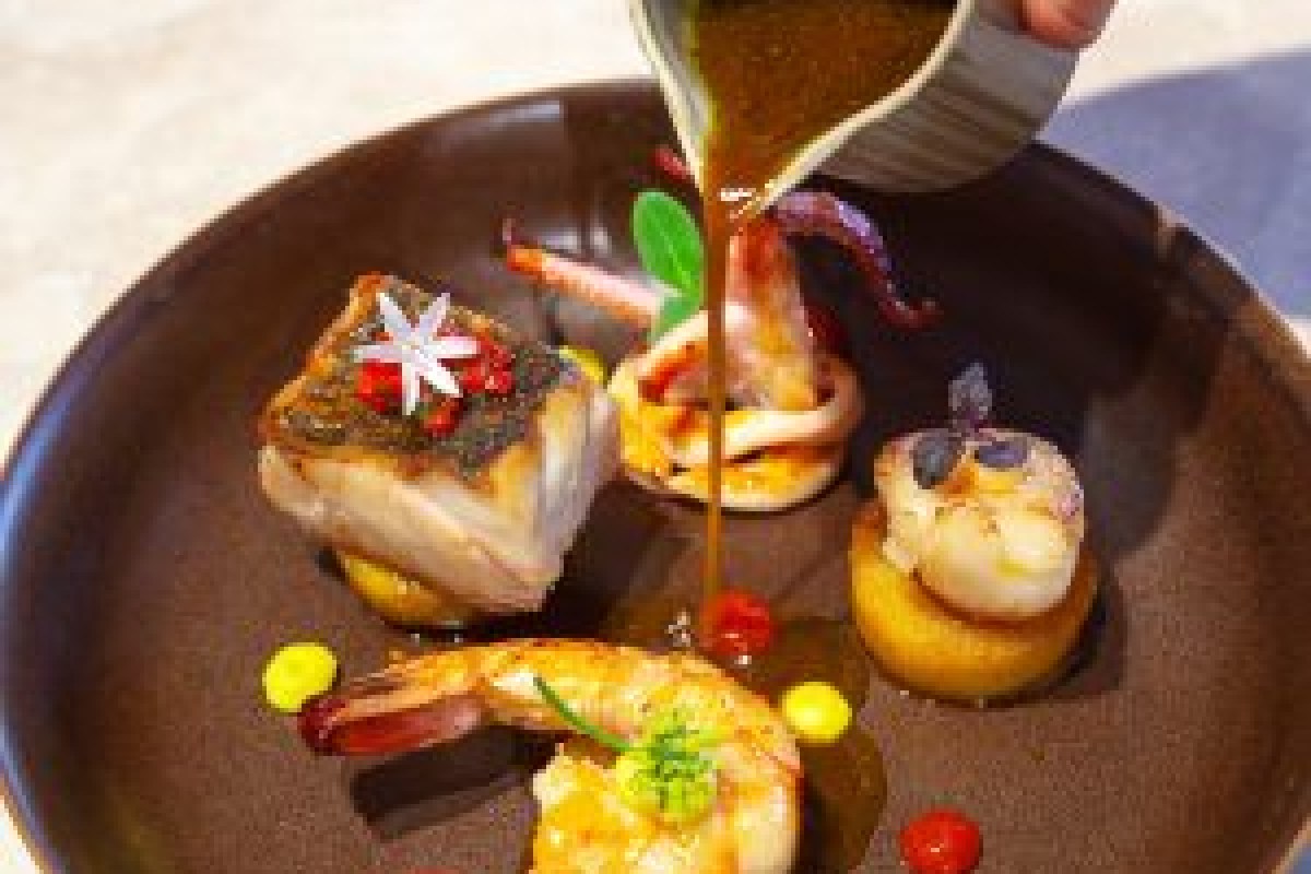 Gourmet seafood plate with fish, shrimp, scallop and octopus, drizzled with dark sauce, elegant plating