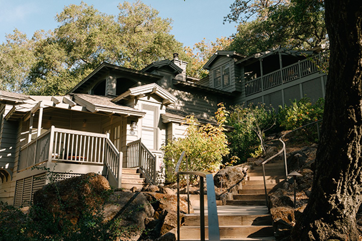 Exterior view of a shingled lodge cottage with staircase through rocky, wooded hillside