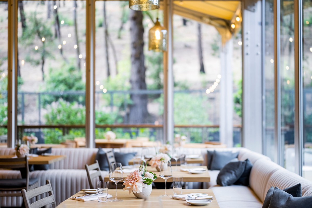 Elegant hotel restaurant interior with plush banquette seating, set tables, and large windows overlooking trees