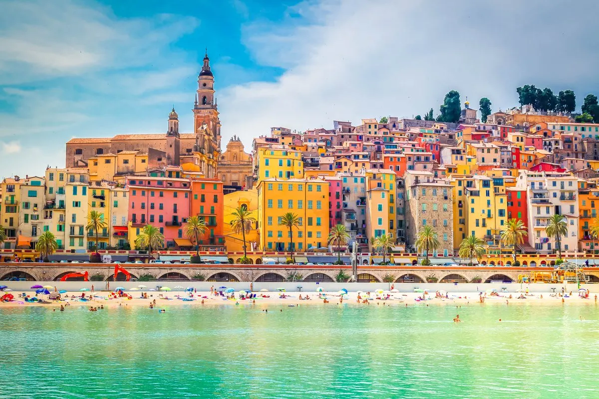 The old town of Menton, with its pastel-coloured buildings and the basilica's tower rising above the beach and the turquoise sea