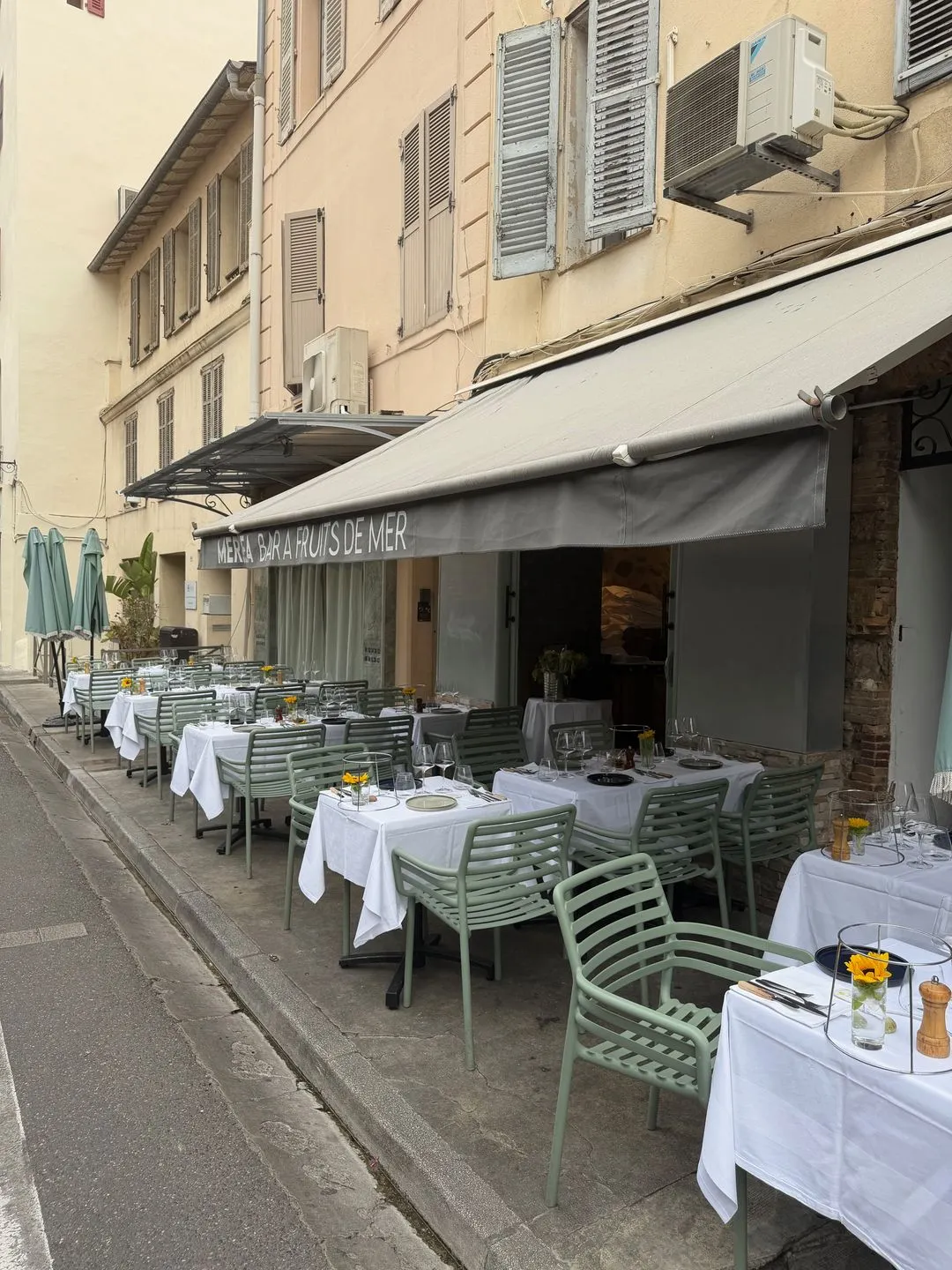 Mersea's tables with white cloths set out along Cours Masséna under grey awnings, in the morning light of Vieil Antibes