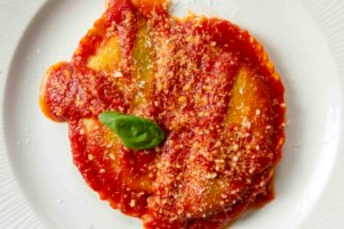 Plate of ravioli covered in tomato sauce with a basil leaf garnish