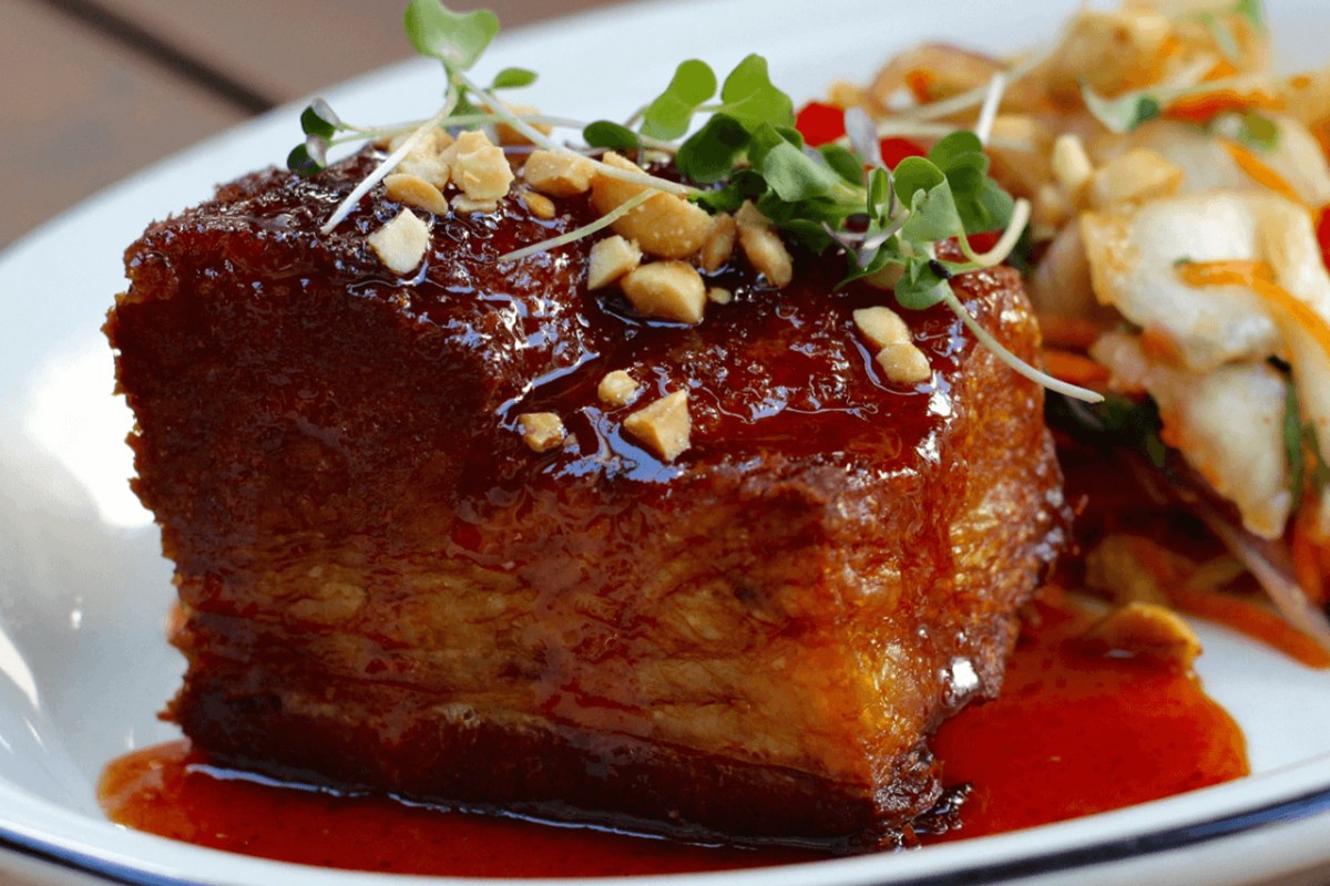 Close-up of glazed pork belly dish topped with crushed peanuts and microgreens on a white plate