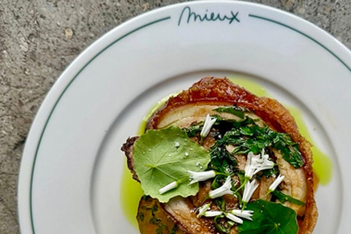 Plated dish of crispy pork belly with herbs and edible flowers on a plate branded 'Mieux'