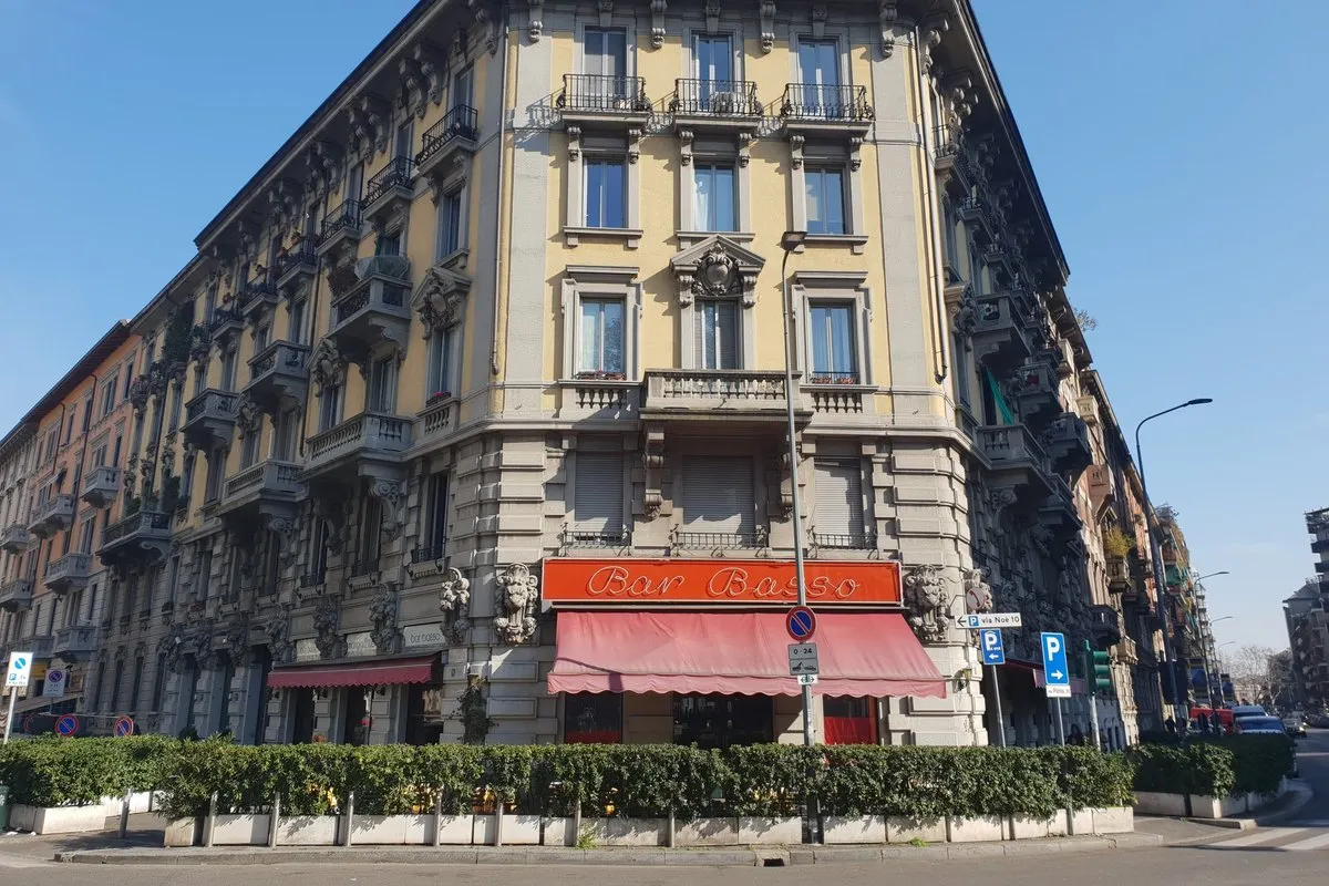 Bar Basso with its orange sign and awning on the ground floor of a Liberty-style corner building on Via Plinio, Milan