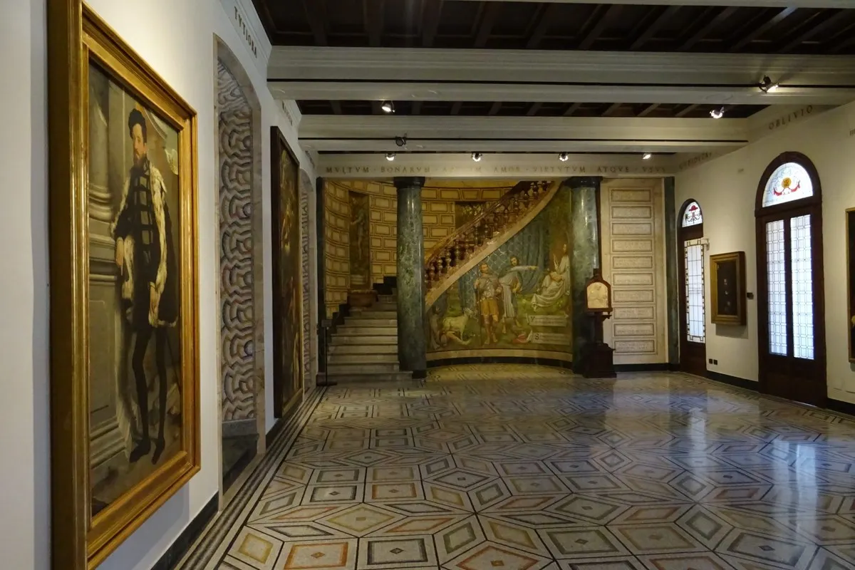 The Sala dell'Esedra in the Pinacoteca Ambrosiana, Milan, with an inlaid marble floor, a mosaic-clad staircase between green columns and large paintings on the walls