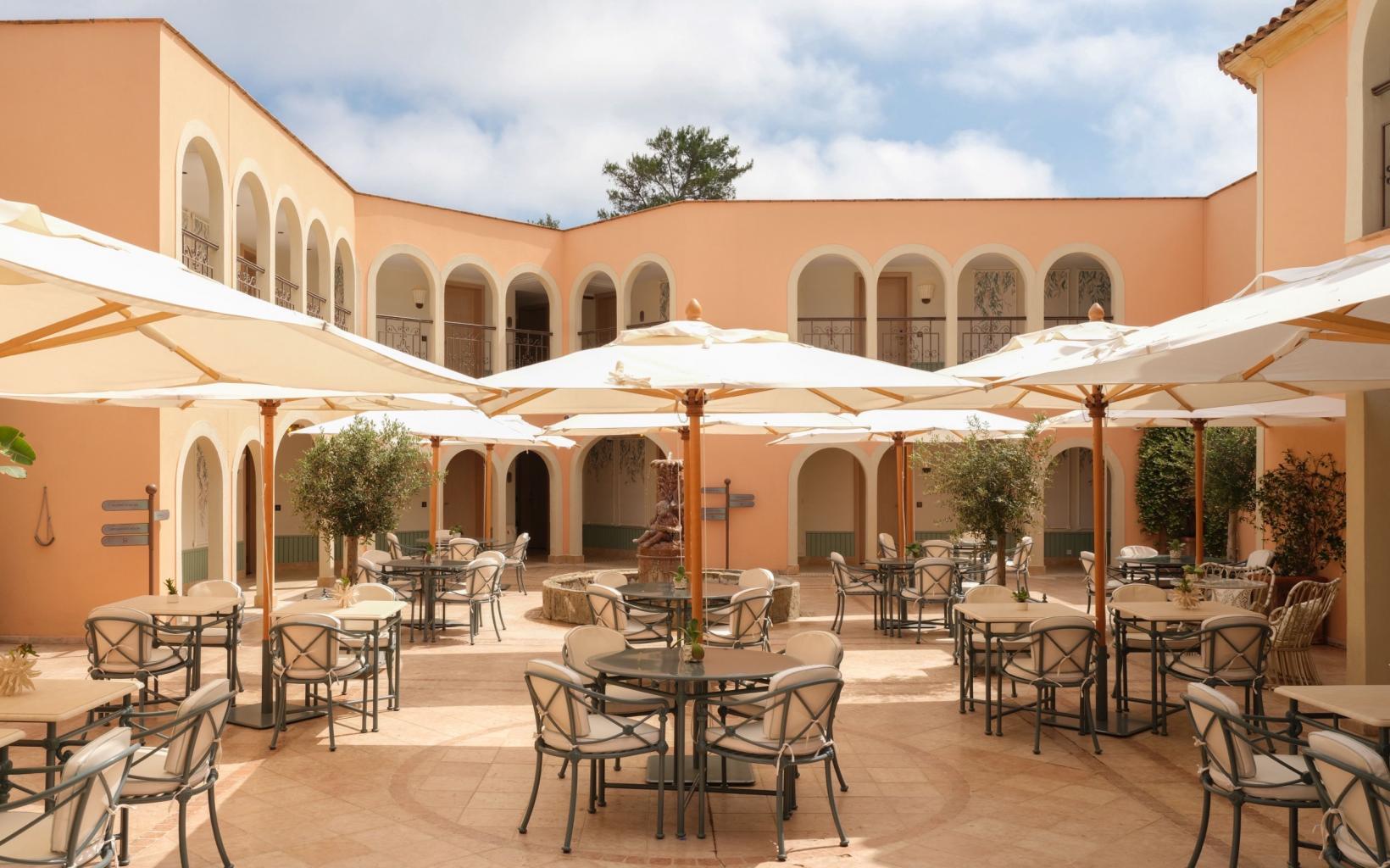 The arcaded patio terrace of Villa Miraé on Cap d'Antibes, with cream parasols over laid tables and olive trees in pots