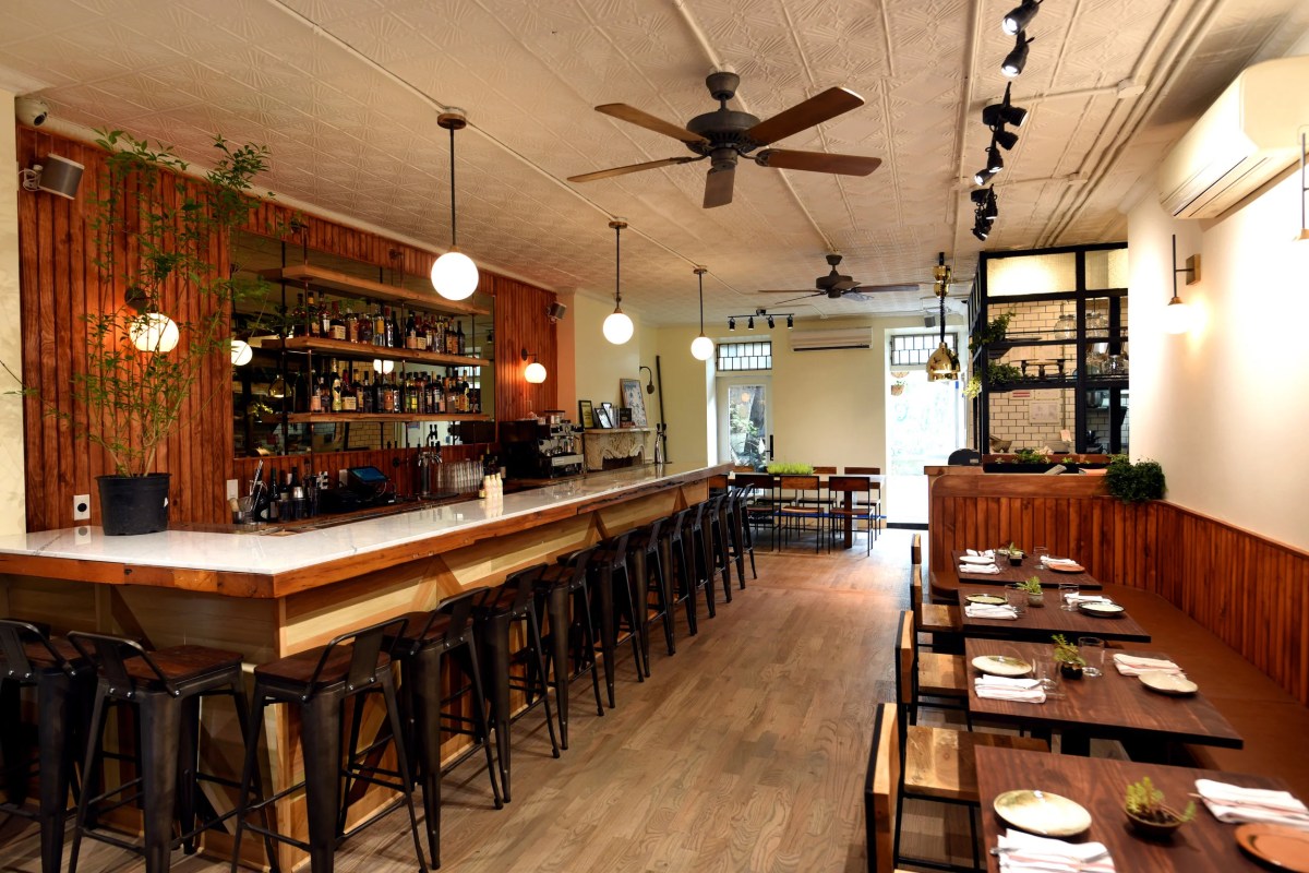 Restaurant interior with long wooden bar, stools, and dining tables along the wall