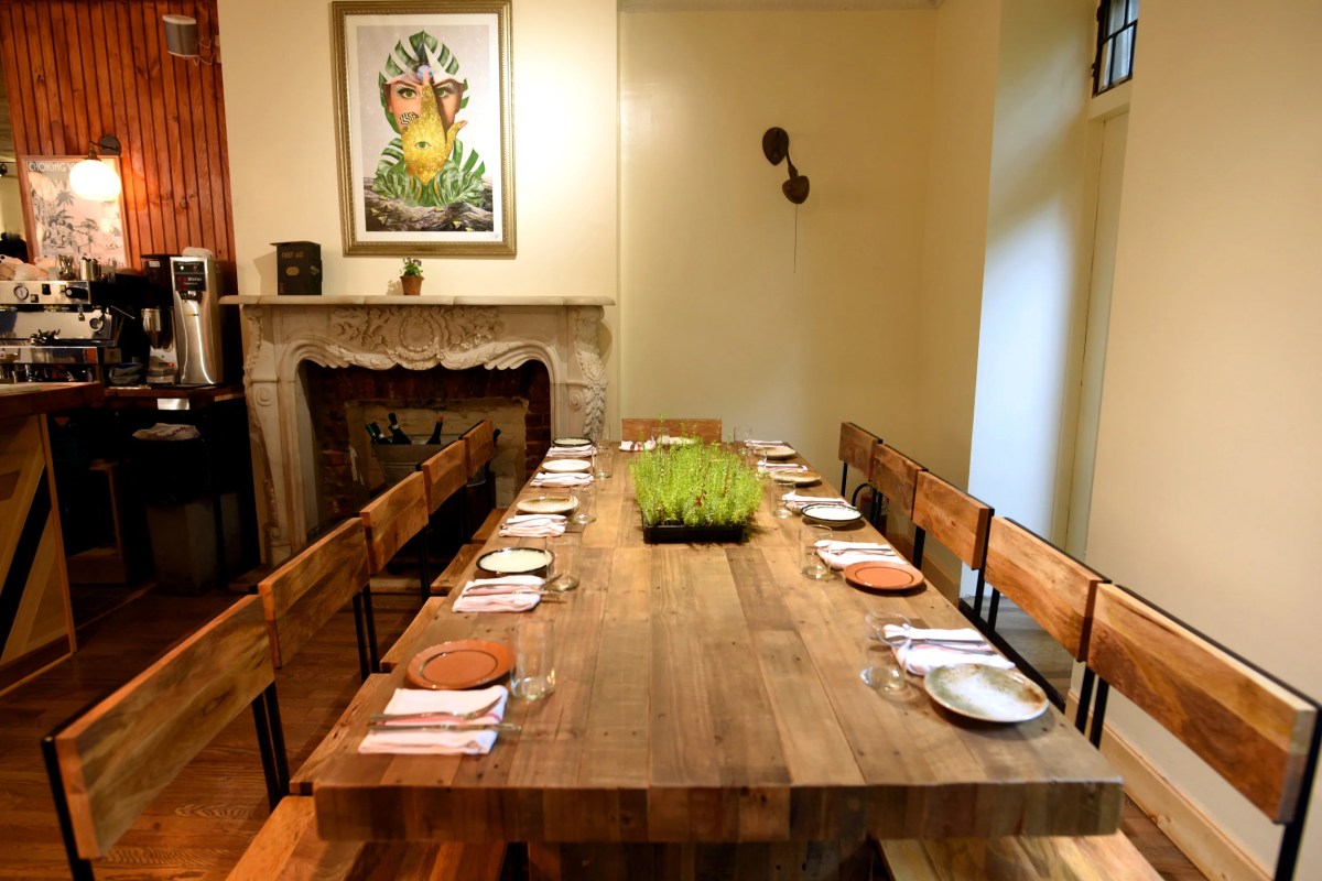 Dining room long communal table set with plates, with ornate fireplace mantel in background