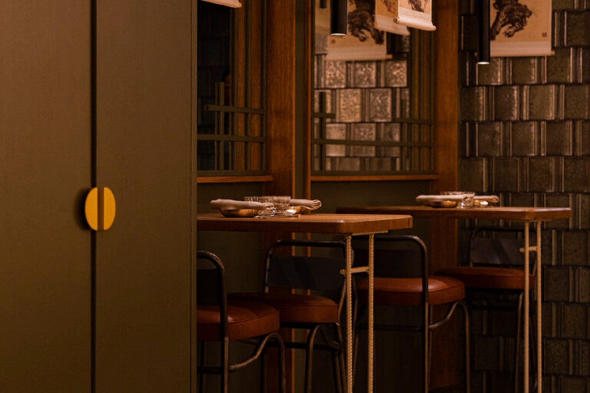 View through doorway into Mojju dining area with tiled wall, hanging scroll art, and leather bar stools